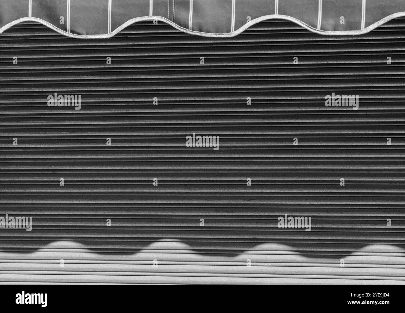 Riflessi delle onde astratte: Ombre illuminate dal sole su tenda metallica a negozio chiuso con motivo a righe. Foto Stock