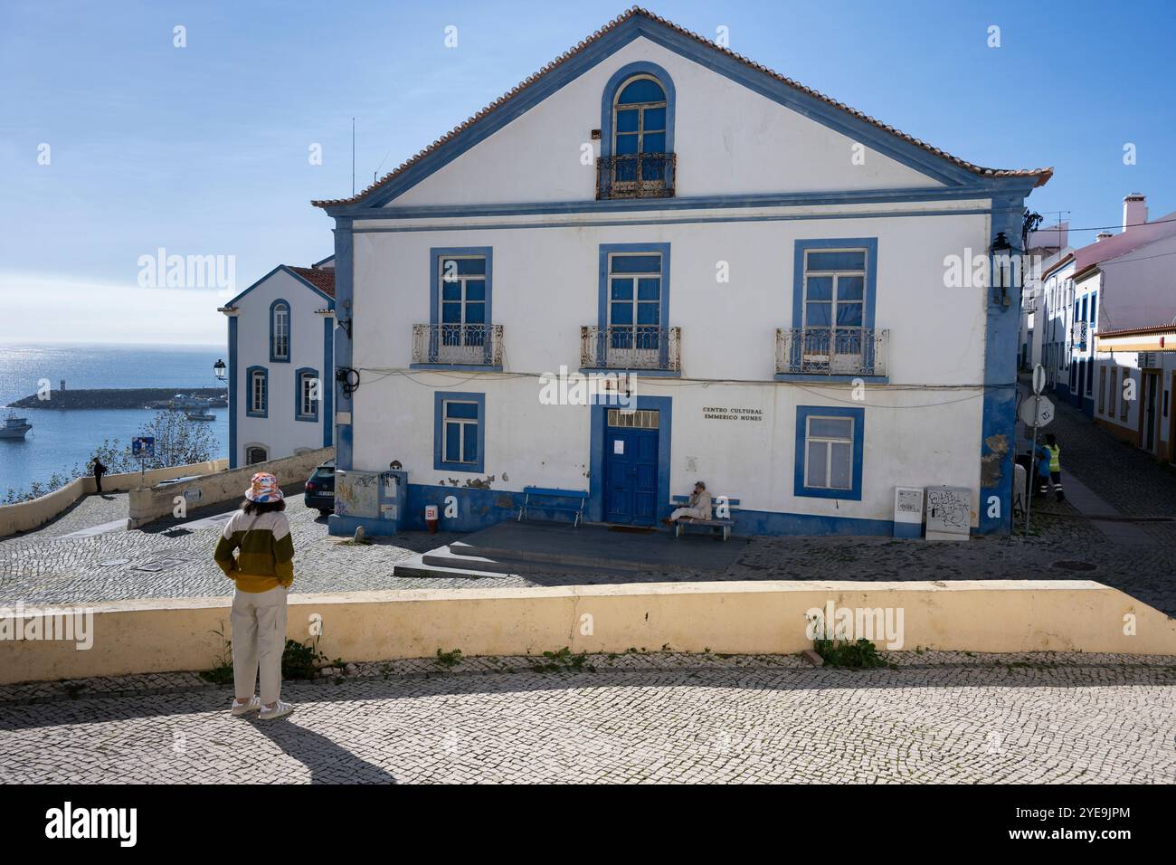 Donna si erge davanti a una casa bianca e blu nella città costiera di Sines nella regione Alentejo del Portogallo; Sines, Setubal, Portogallo Foto Stock