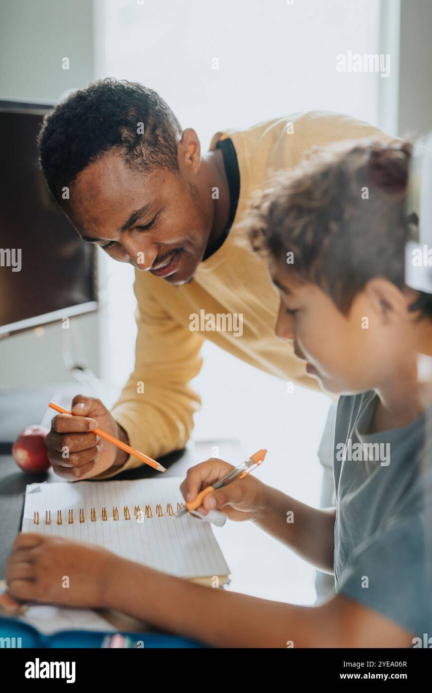 Padre sorridente che aiuta figlio a fare i compiti a casa Foto Stock