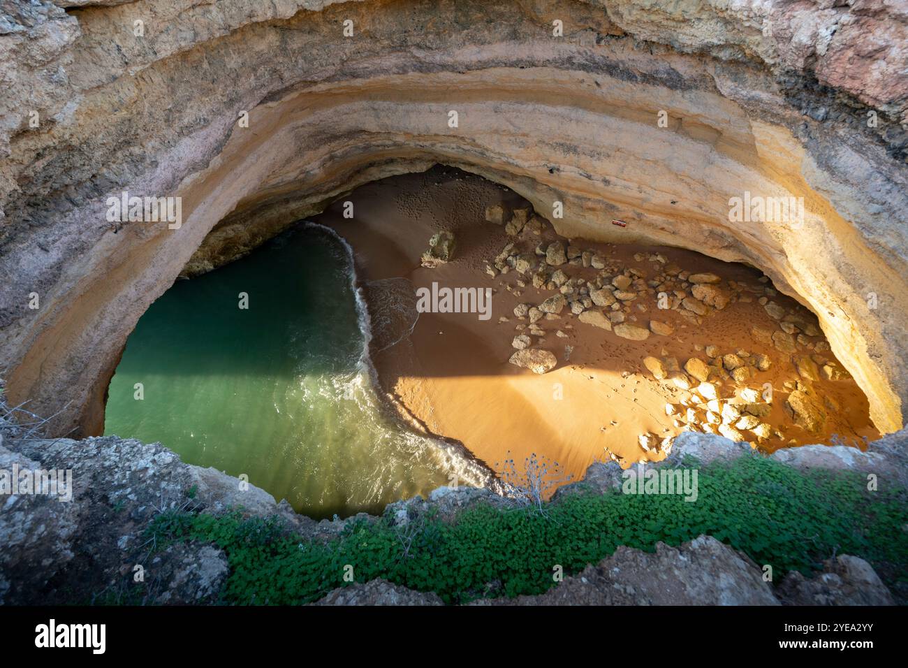 Vista ad alto angolo della calda luce del tramonto sulla sabbia, sulle rocce e sull'acqua alla Grotta di Benagil lungo la costa del Portogallo; Lagoa, Faro, Portogallo Foto Stock