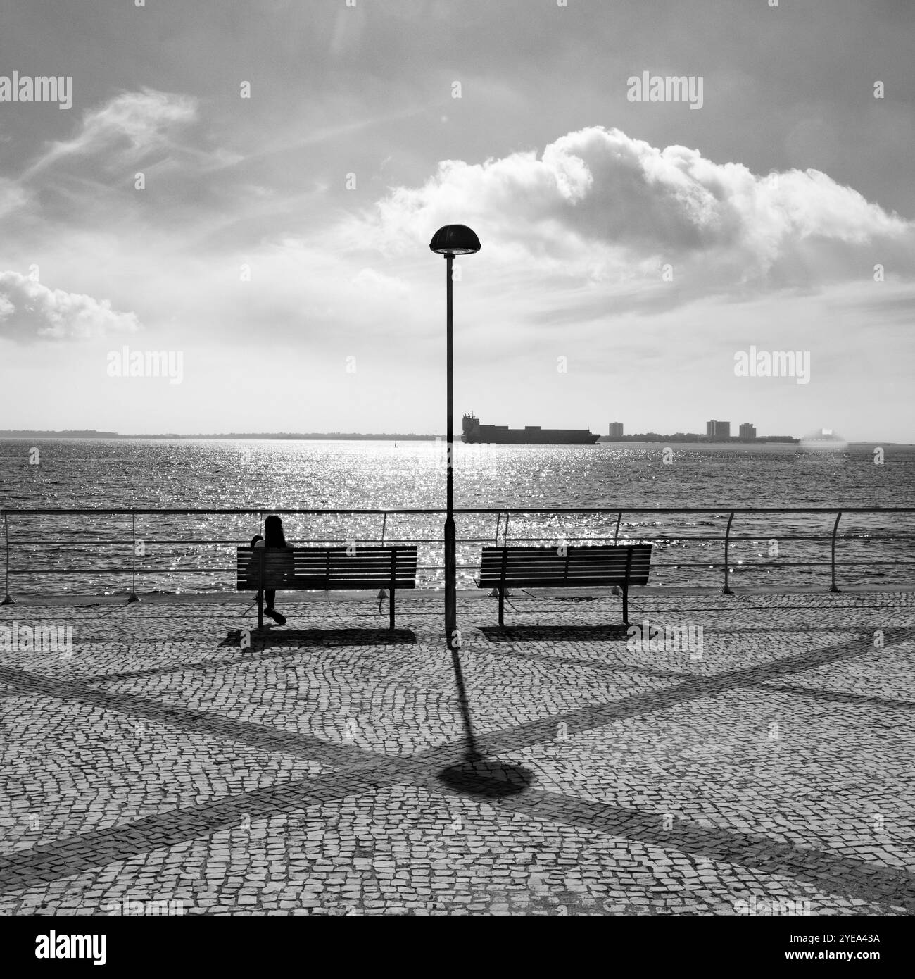 Posti a sedere lungo il lungomare con vista sul trafficato porto di Setubal, Portogallo. Setubal è un porto e una città industriale affollati che vanta un'ampia... Foto Stock