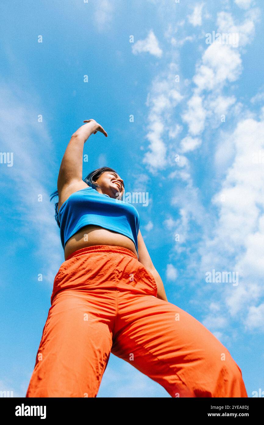 Vista dall'angolo basso di una donna felice che balla sotto il cielo nuvoloso Foto Stock