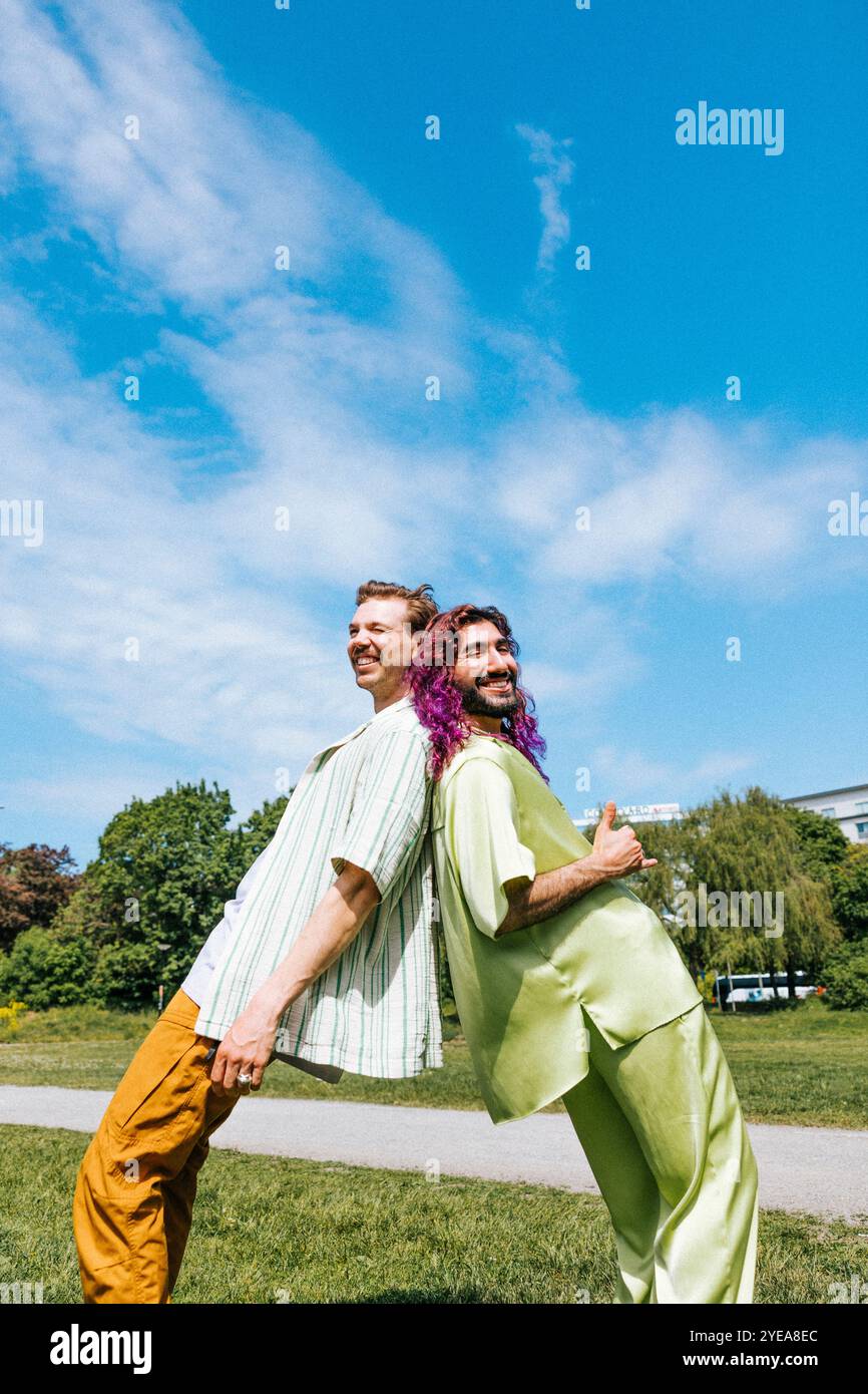 Amici maschili giocosi che si appoggiano uno contro l'altro nel parco pubblico sotto il cielo nuvoloso Foto Stock