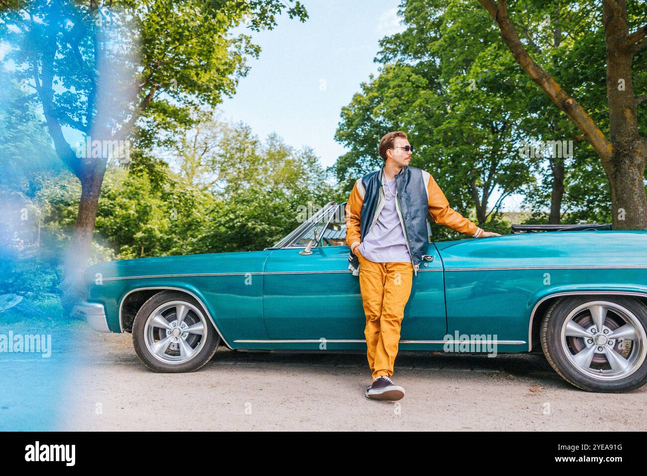 Uomo alla moda con la mano in tasca in piedi vicino a un'auto d'epoca al parcheggio Foto Stock