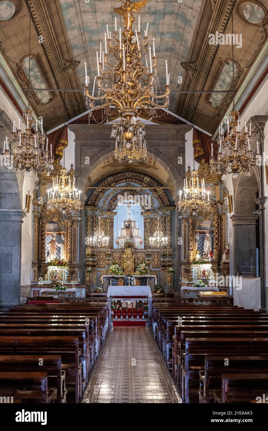 Interno di una chiesa con altare ornato e lampadari, una navata centrale e pali di legno; Camara de Lobos, Madeira, Portogallo Foto Stock