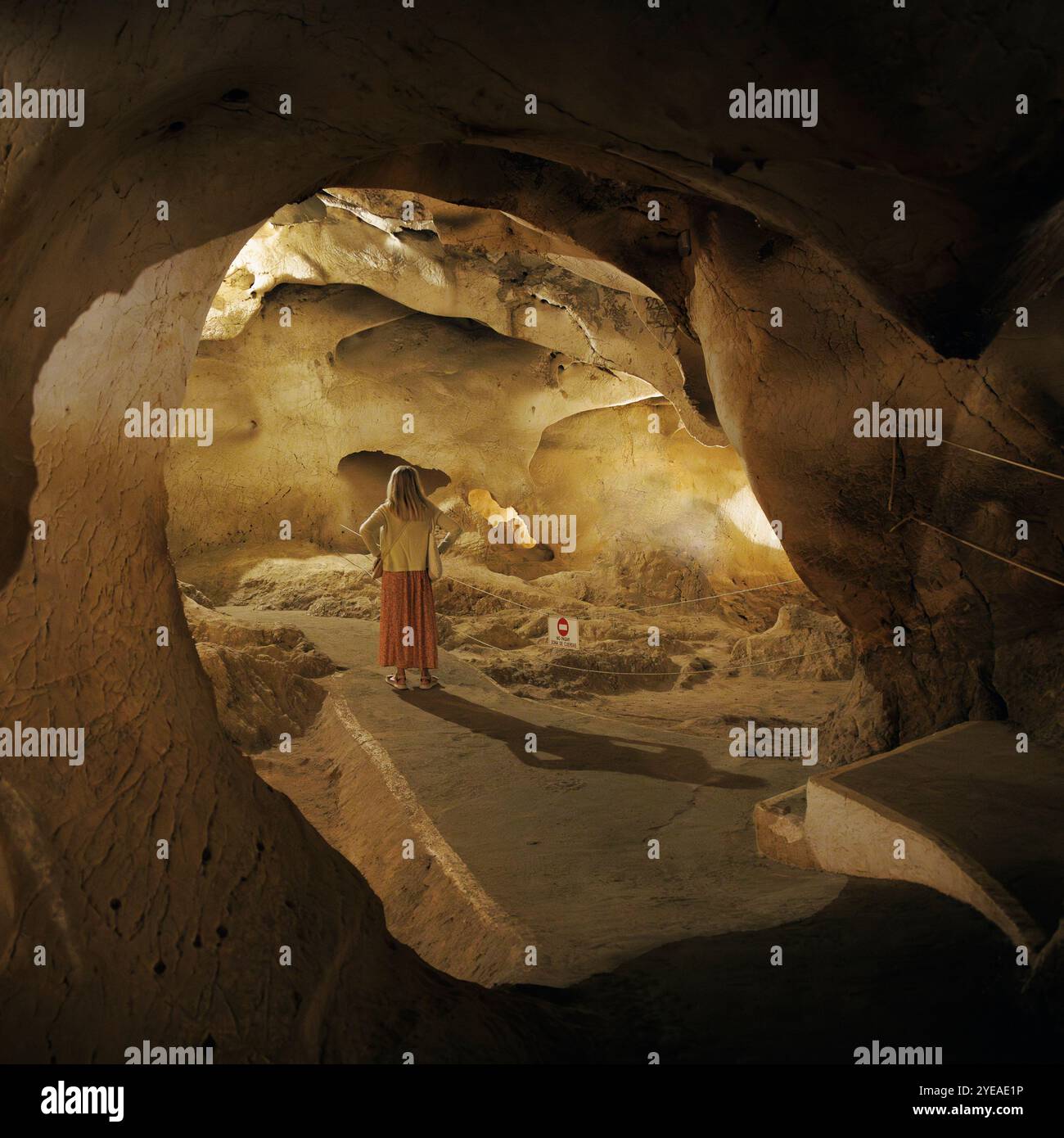 Vista posteriore di una donna che si trova su un sentiero in una grotta marina illuminata, Treasure Cave, a Malaga, Spagna Foto Stock