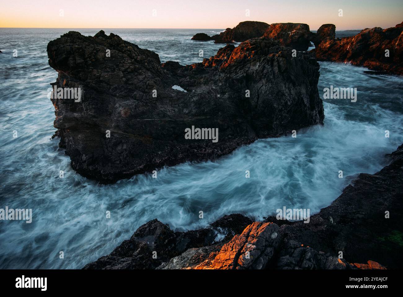 Vista spettacolare del surf spumeggiante e delle onde che oscillano e si infrangono sulla costa rocciosa delle formazioni rocciose e dell'isolotto a Mendocino Headlands al tramonto Foto Stock