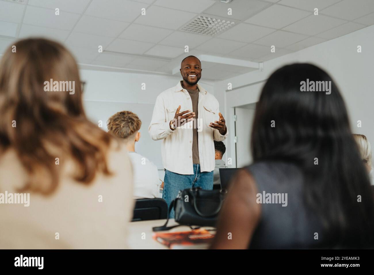 Felice insegnante maschile che gestisce mentre insegna agli studenti delle scuole superiori in classe Foto Stock