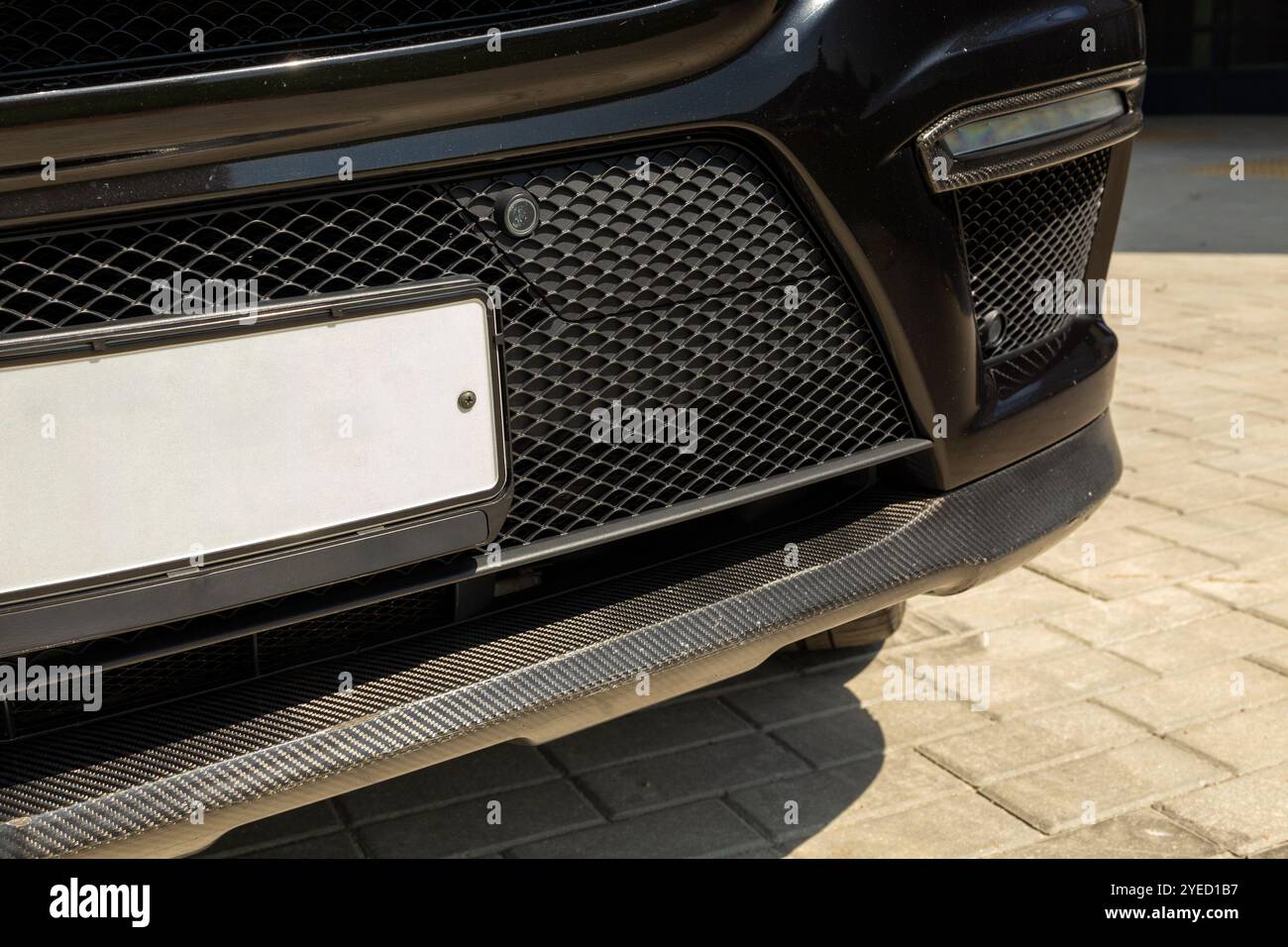 Il paraurti anteriore di un'auto nera presenta sorprendenti sovrapposizioni in carbonio, che uniscono estetica sportiva e design all'avanguardia per un look automobilistico di qualità superiore. Foto Stock