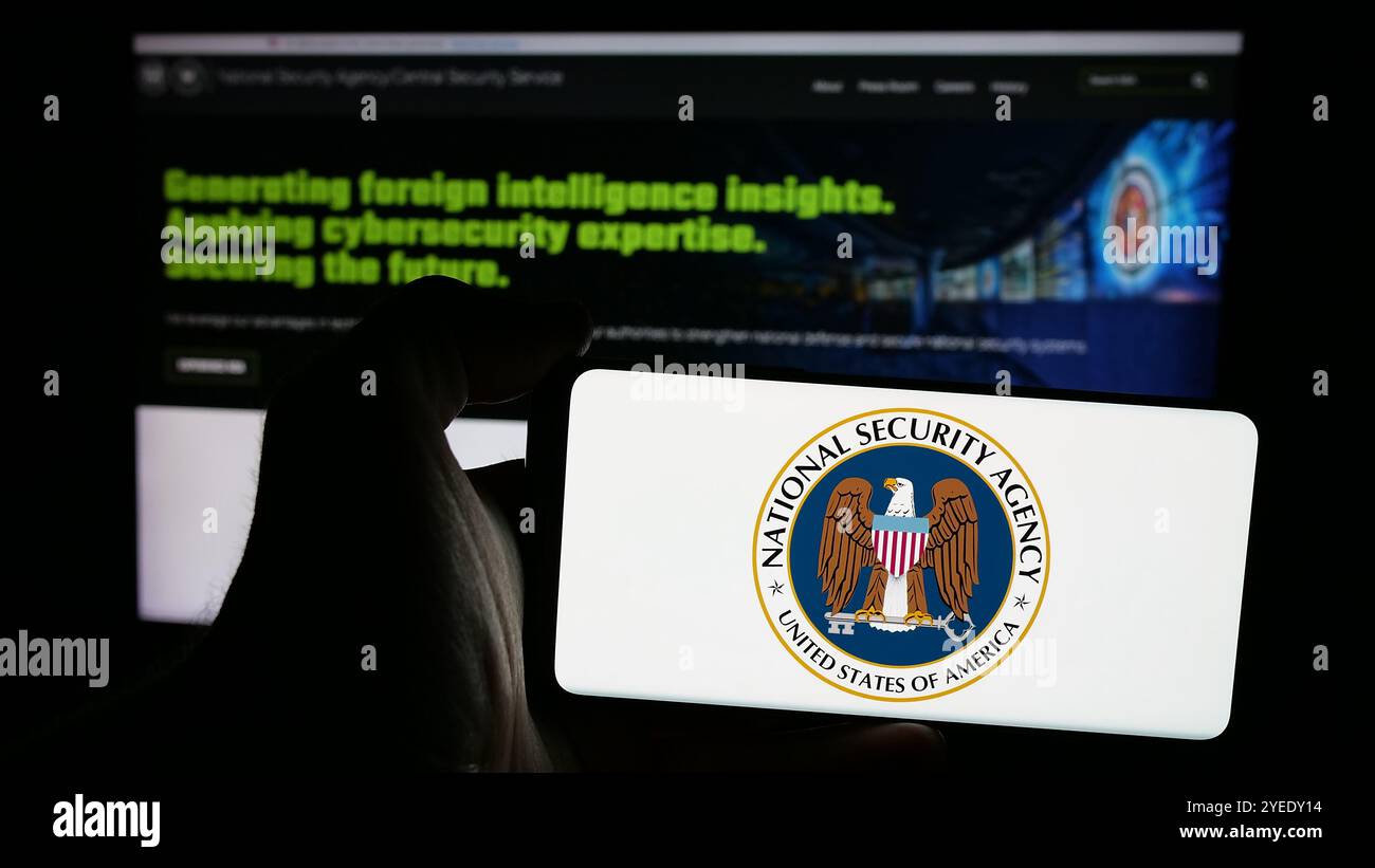 Persona che possiede uno smartphone con il logo della National Security Agency (NSA) sullo schermo di fronte al sito web. Mettere a fuoco il display del telefono. Foto Stock