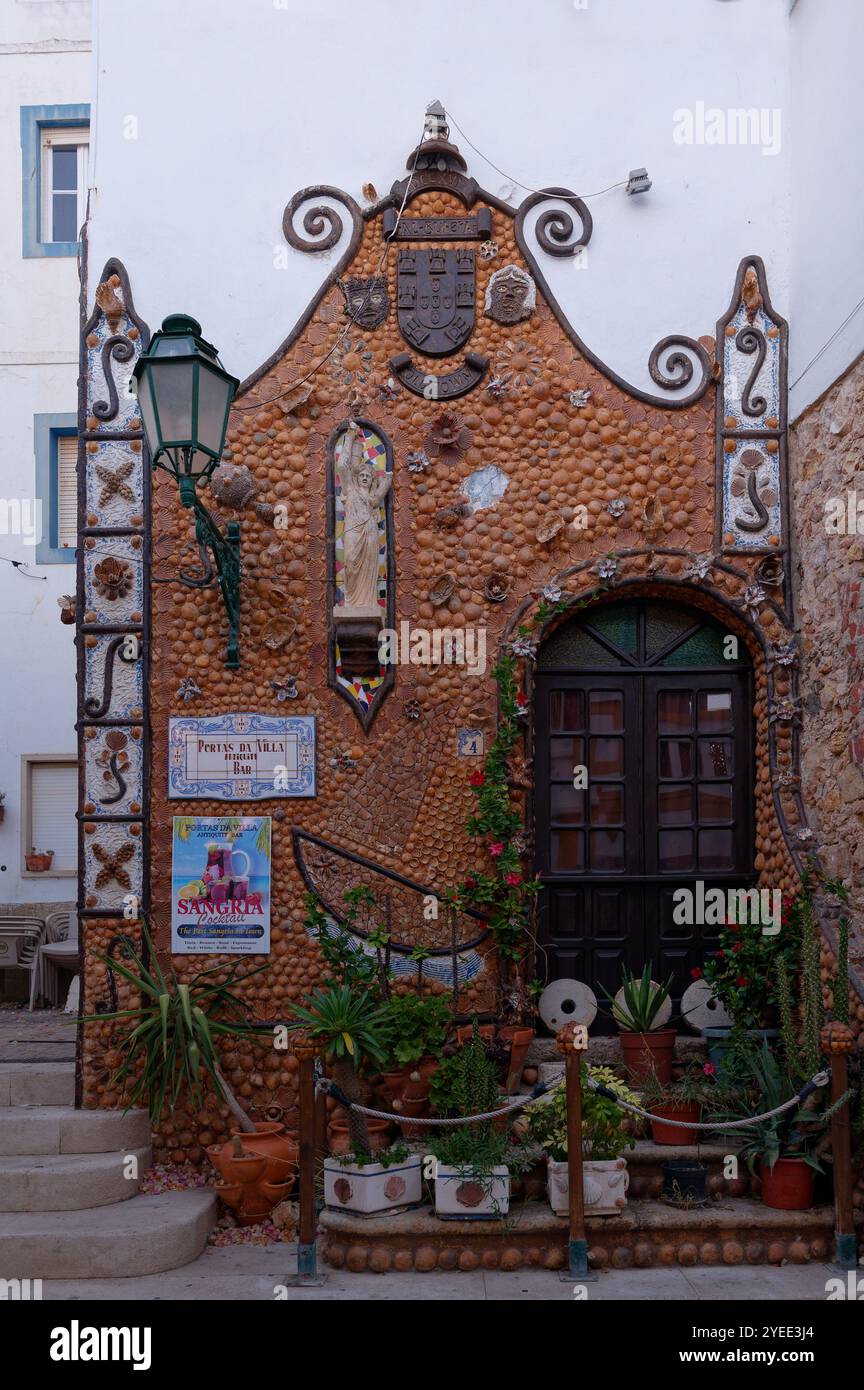 Affascinante facciata coperta di conchiglie di un bar locale chiamato Portas da Vila Bar, decorata con piante e motivi costieri Foto Stock