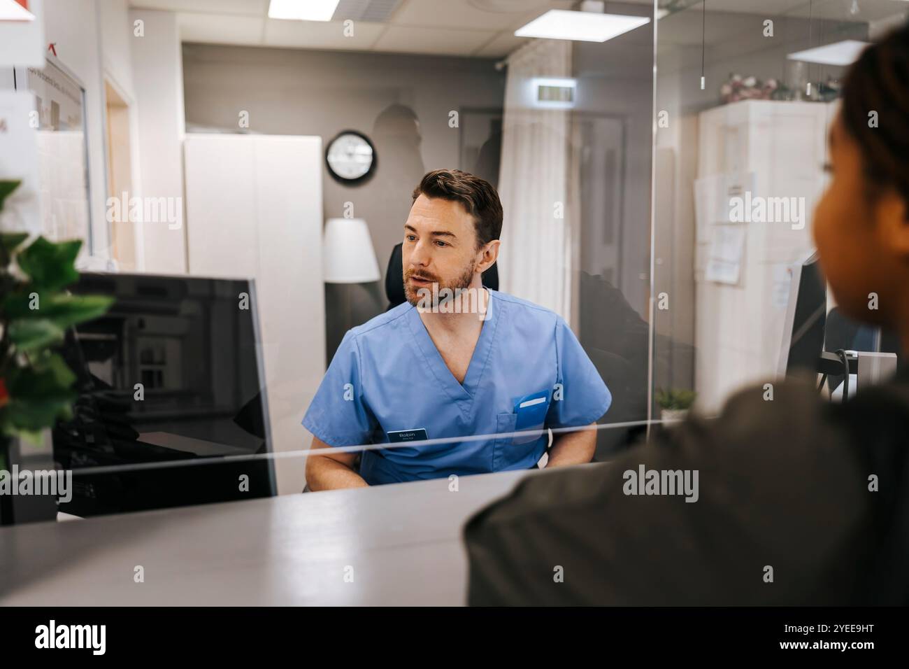 Receptionist maschile che guarda il computer e assiste il paziente in piedi in ospedale Foto Stock