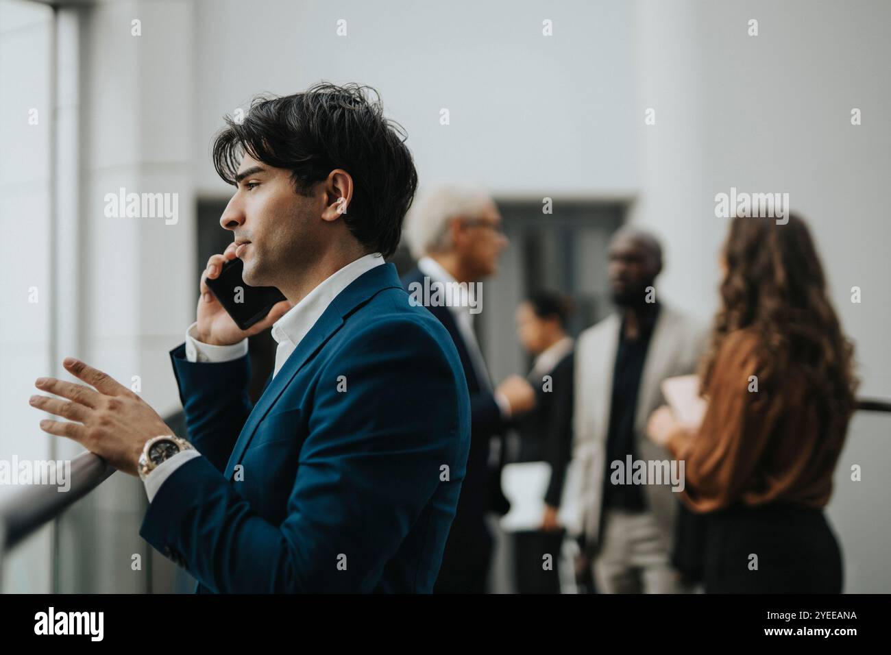 Vista laterale di un giovane uomo d'affari che parla con uno smartphone tramite ringhiera Foto Stock