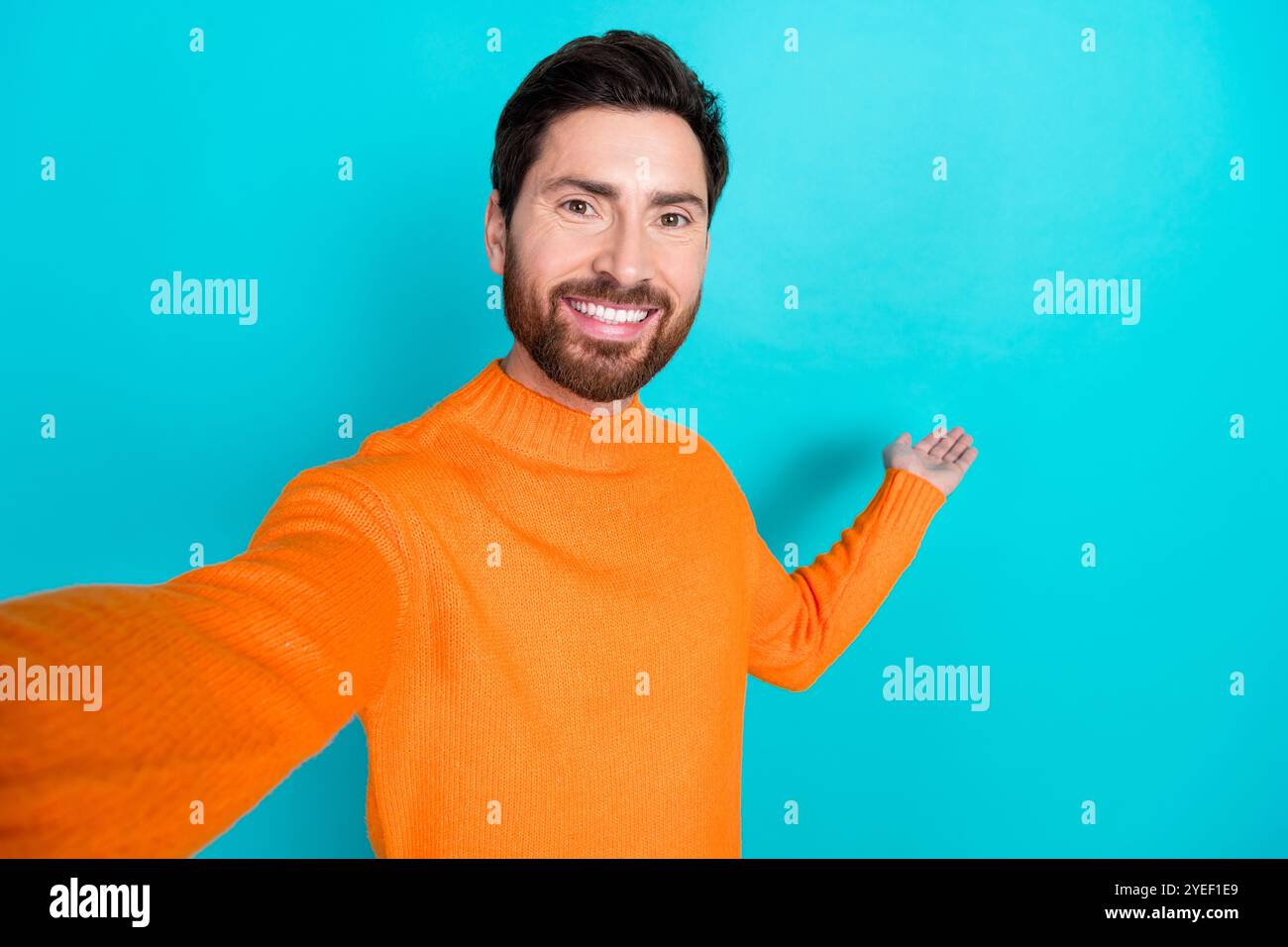 Foto di un affascinante blogger che indossa abiti alla moda arancioni che tengono uno spazio vuoto isolato su sfondo di colore ciano Foto Stock