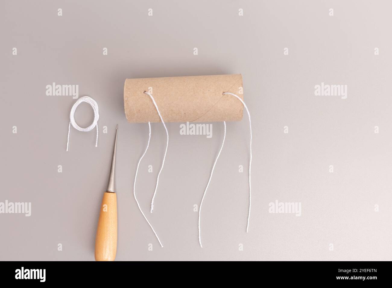 Tubo in rotolo di carta igienica con inserimento di una corda attraverso i fori, parte del progetto fai da te, momento nel processo di creazione, evidenziando l'uso di S. Foto Stock