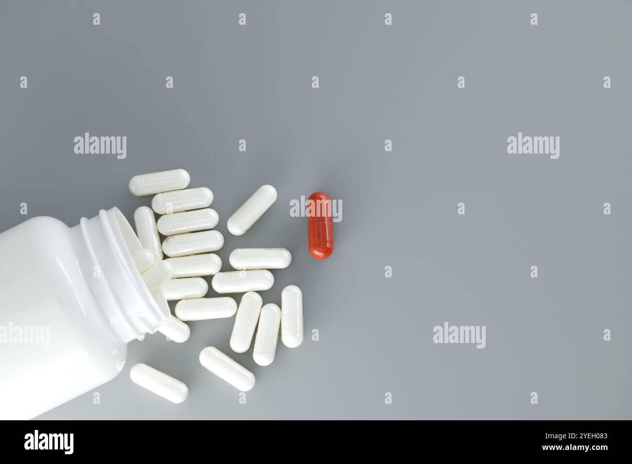 Flacone bianco rovesciato con il suo contenuto pillole o capsule bianche, versato su sfondo grigio. Tra queste pillole bianche, un re solitario Foto Stock