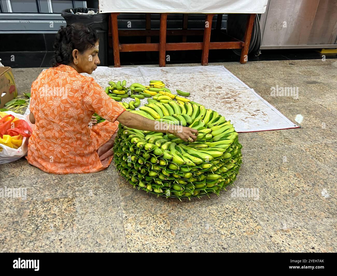 All'interno del tempio indù, la donna indiana sta impilando le banane in forma circolare per offrirle agli dei. Tempio di Sri Thendayuthapani. Singapore. - Immagine stock catturata con smartphone