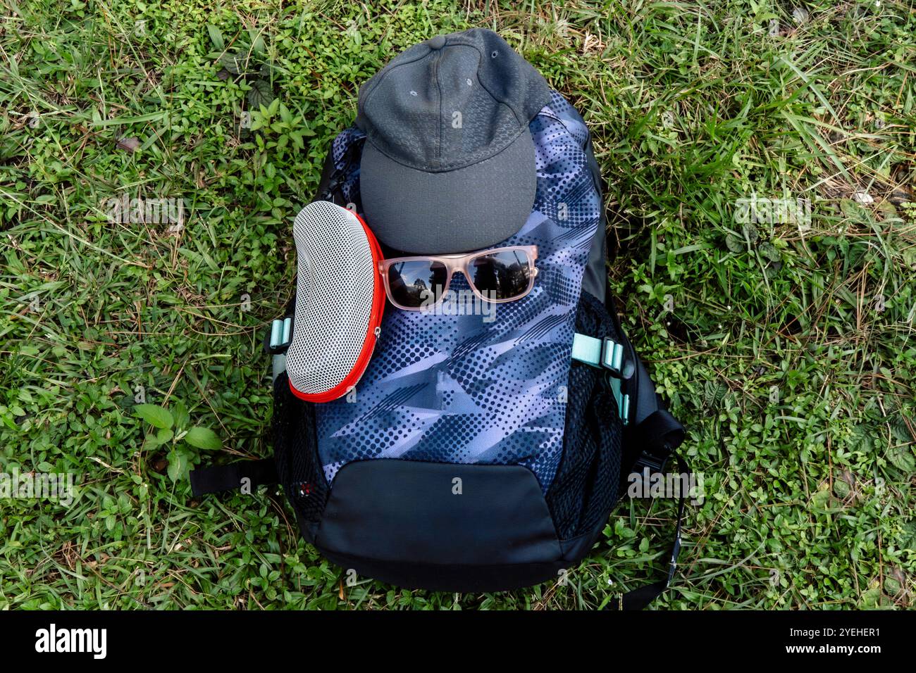 Un cappello e gli occhiali da sole in cima alla borsa da trekking siediti nell'erba con un cappello su di esso allestimento escursionistico Foto Stock