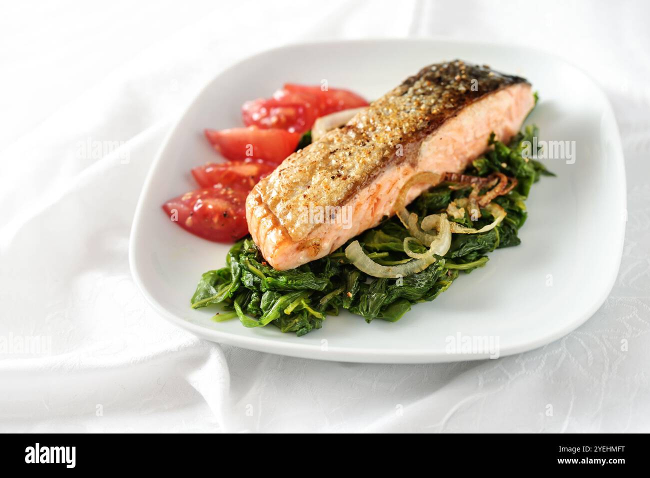 Filetto di salmone arrosto con pelle con verdure di spinaci, cipolle e pomodori, pasto sano per una dieta a basso contenuto di carboidrati su un piatto bianco e tovaglia, copia spa Foto Stock