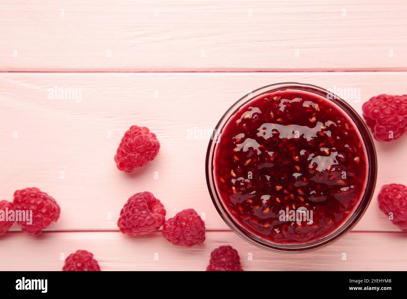 Marmellata di lamponi in un recipiente con frutti di bosco su sfondo rosa. Vista dall'alto Foto Stock