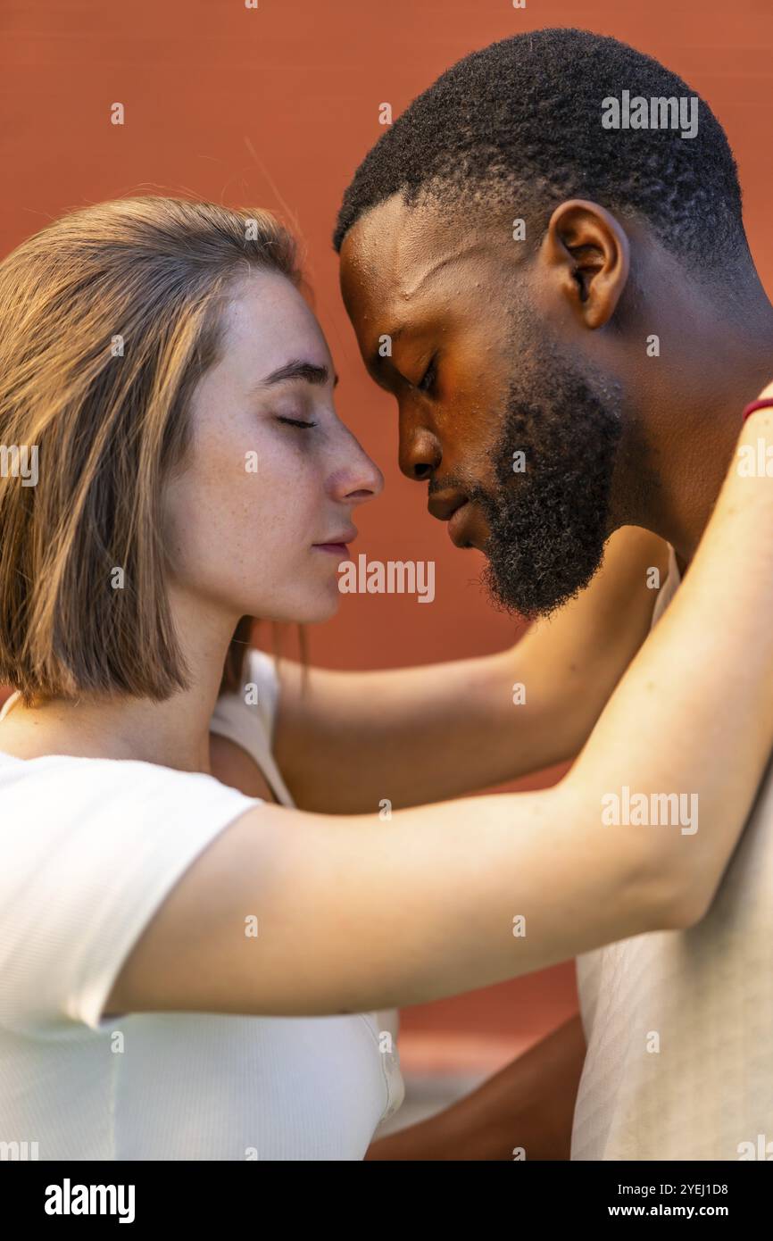Foto verticale di una giovane coppia multietnica che condivide un momento romantico abbracciando faccia a faccia Foto Stock