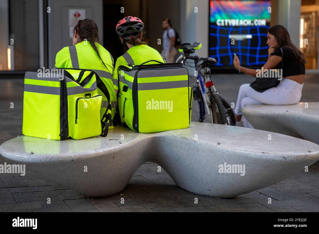 Due corrieri in giacche gialle ad alta visibilità con i loro sacchetti di consegna appoggiati accanto a loro. Foto Stock