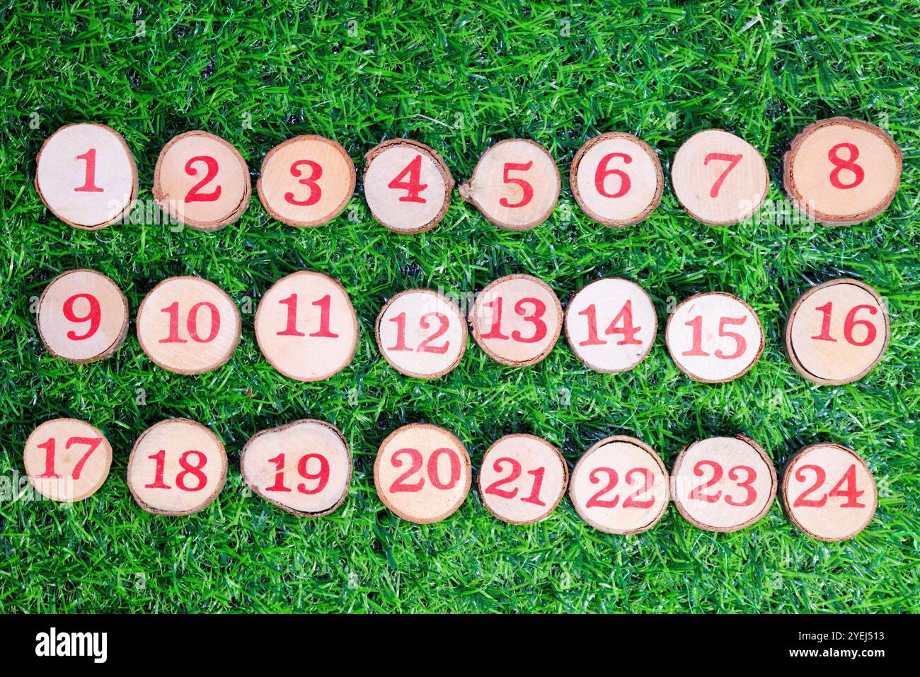 Numeri rossi da 1 a 24 visualizzati su piccoli bottoni di legno su uno sfondo verde brillante, adatti per l'avvento natalizio. Foto Stock