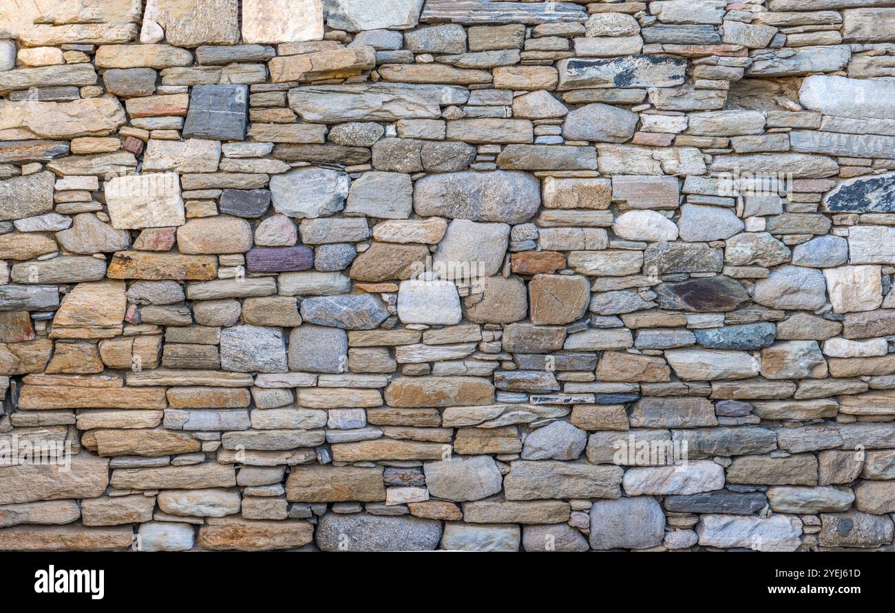 Sfondo strutturato e senza cuciture di un antico muro di pietra con pietre di forma e dimensioni diverse Foto Stock