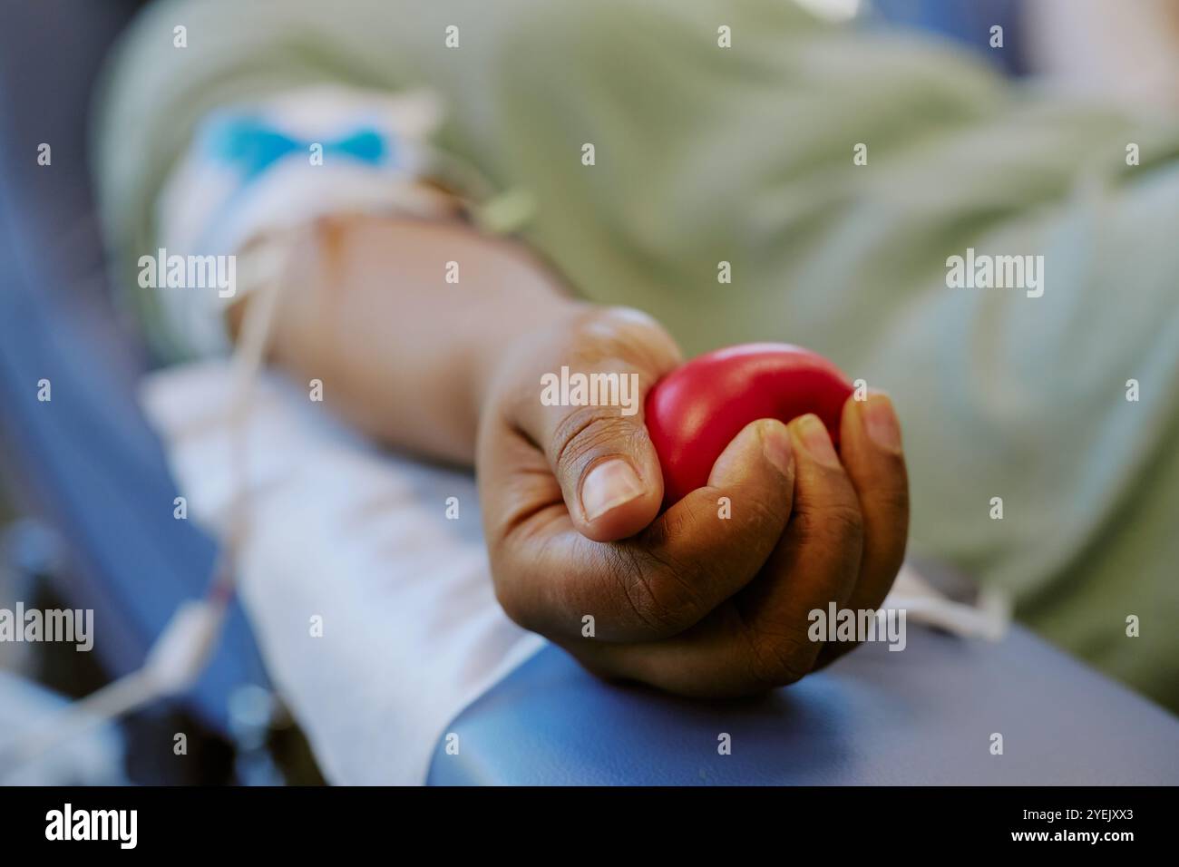 Immagine che mostra un individuo che donava sangue tenendo una palla rossa. Aghi e provette visibili, a indicare il prelievo di sangue Foto Stock
