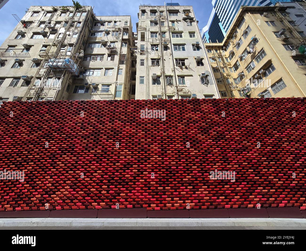 Vecchi edifici residenziali che si nascondono dietro un colorato muro rosso che segna un nuovo complesso di grattacieli a Quarry Bay, Hong Kong. Foto Stock