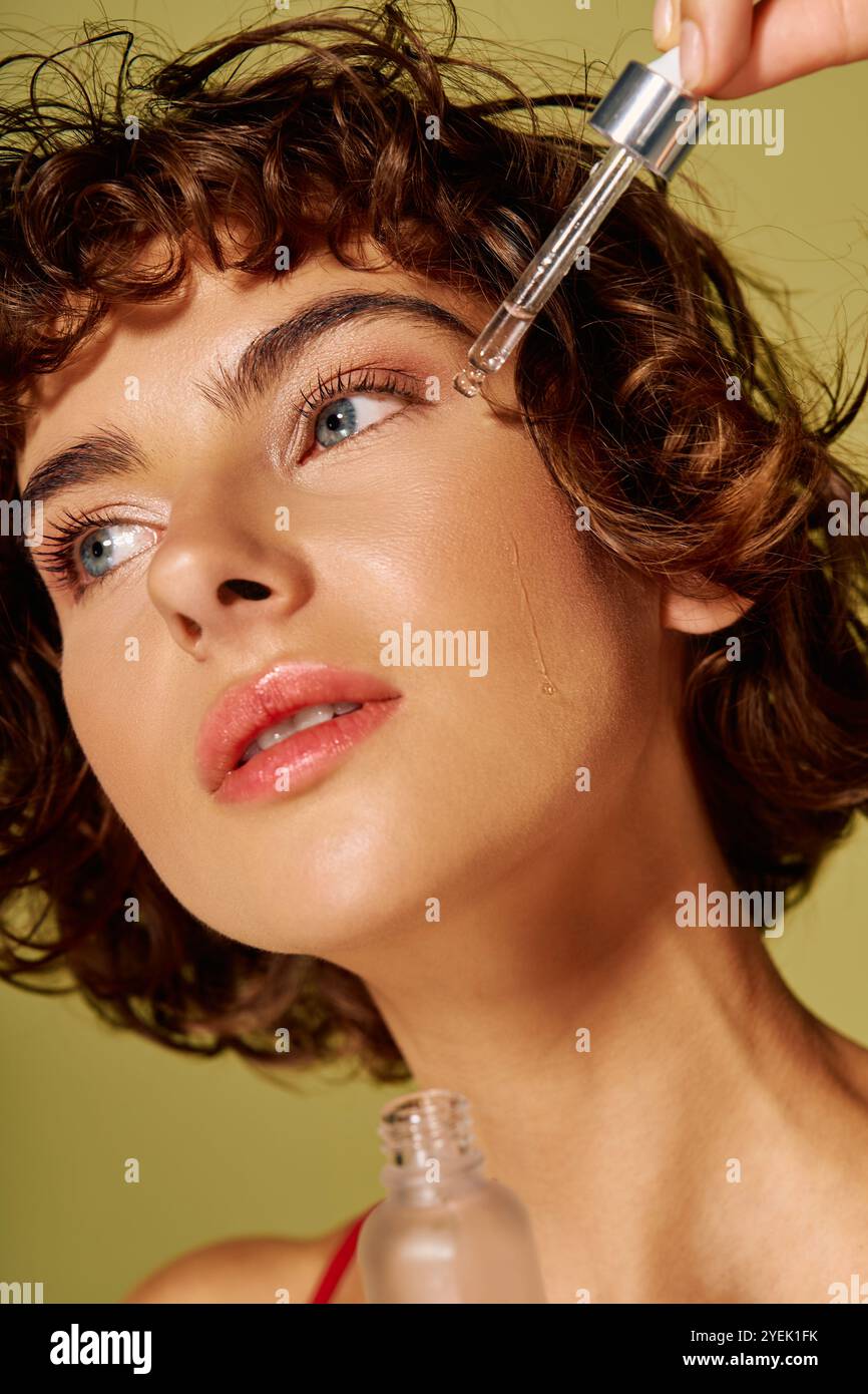 Una giovane donna prova emozioni sentite mentre applica il siero alla sua pelle radiosa. Foto Stock
