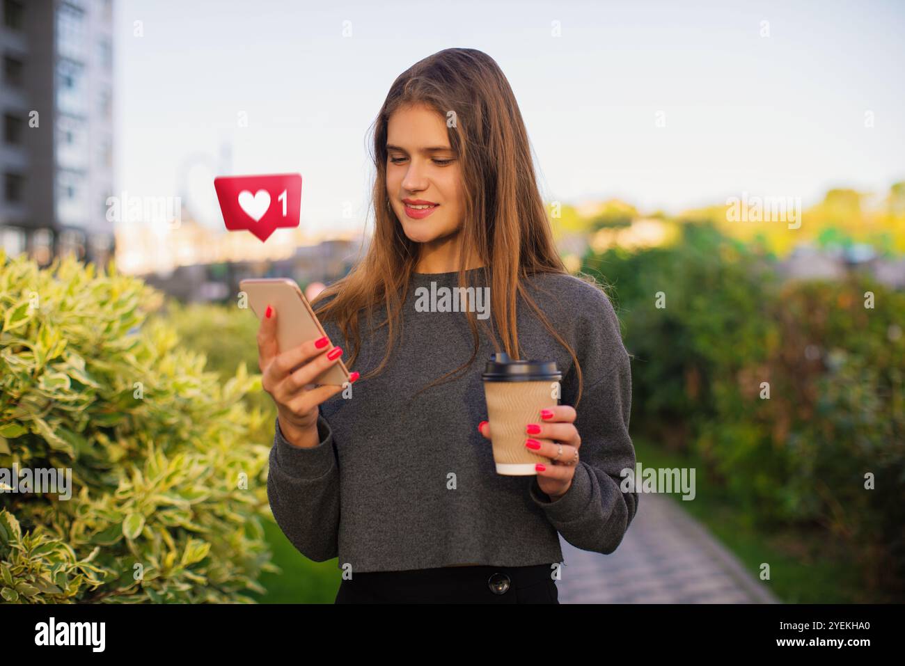 La giovane donna urbana riceve i mi piace sui social media, utilizzando l'app di incontri online sugli smartphone sullo sfondo della città Foto Stock