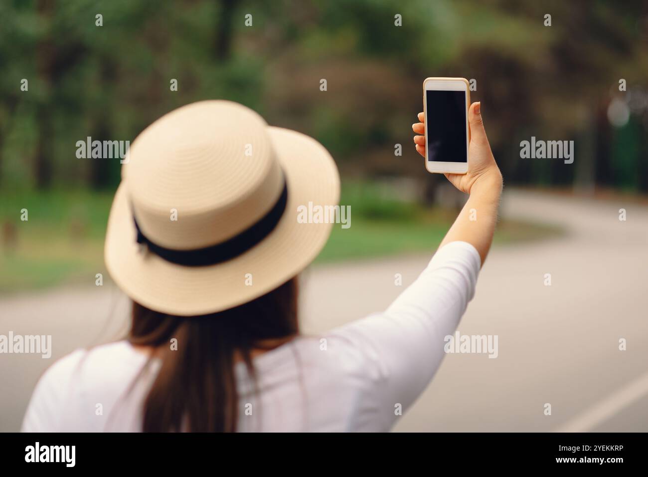 Una donna con il cappello al sole che utilizza uno smartphone moderno in viaggio, vista posteriore all'aperto Foto Stock
