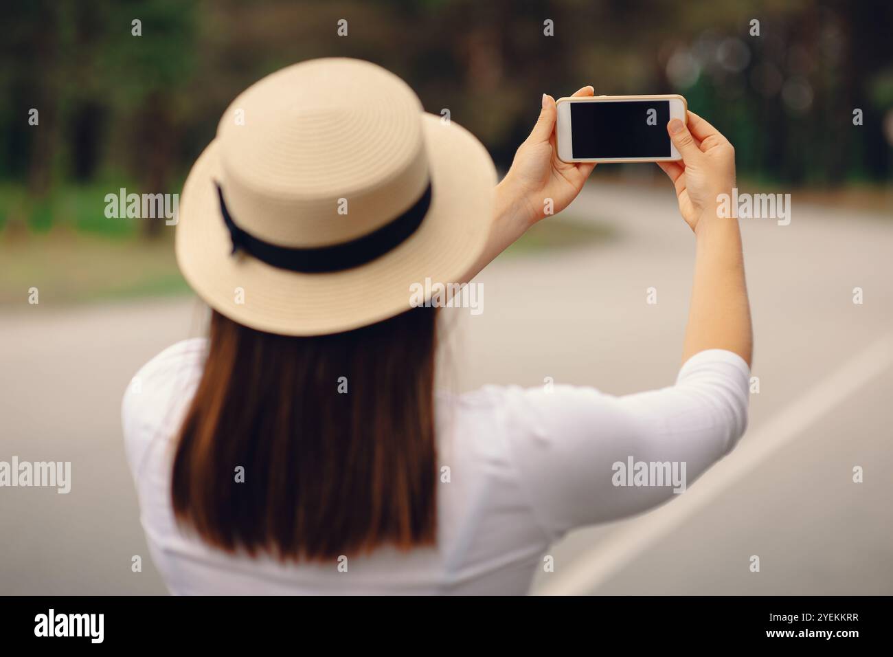 Una donna con il cappello al sole che utilizza uno smartphone moderno in viaggio, vista posteriore all'aperto Foto Stock
