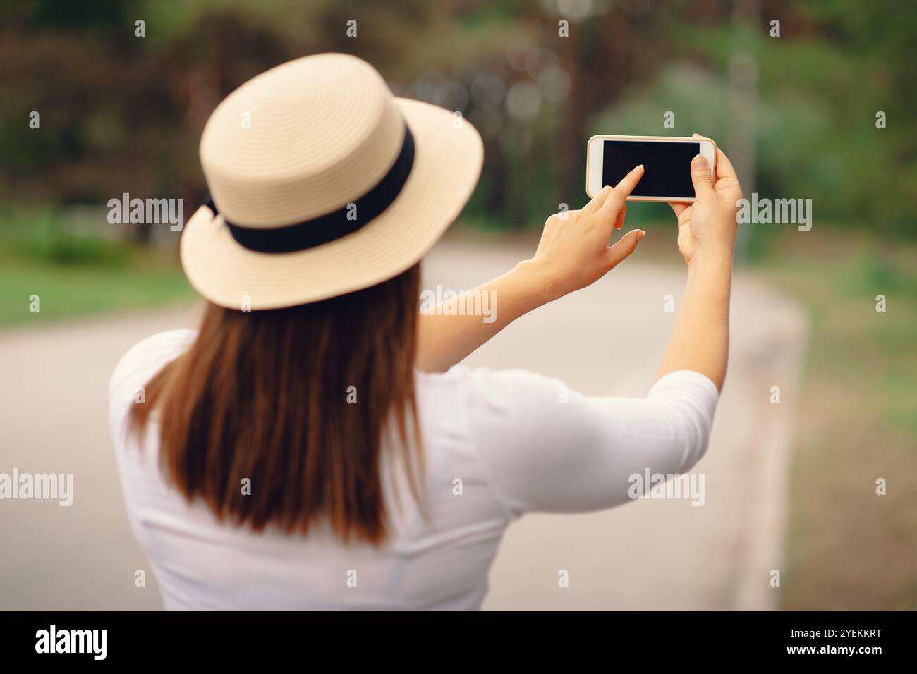 Una donna con il cappello al sole che utilizza uno smartphone moderno in viaggio, vista posteriore all'aperto Foto Stock