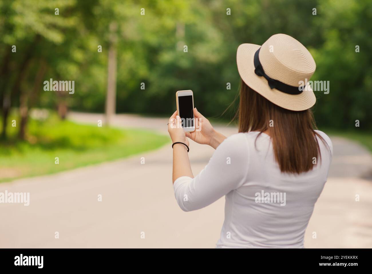 Una donna con il cappello al sole che utilizza uno smartphone moderno in viaggio, vista posteriore all'aperto Foto Stock