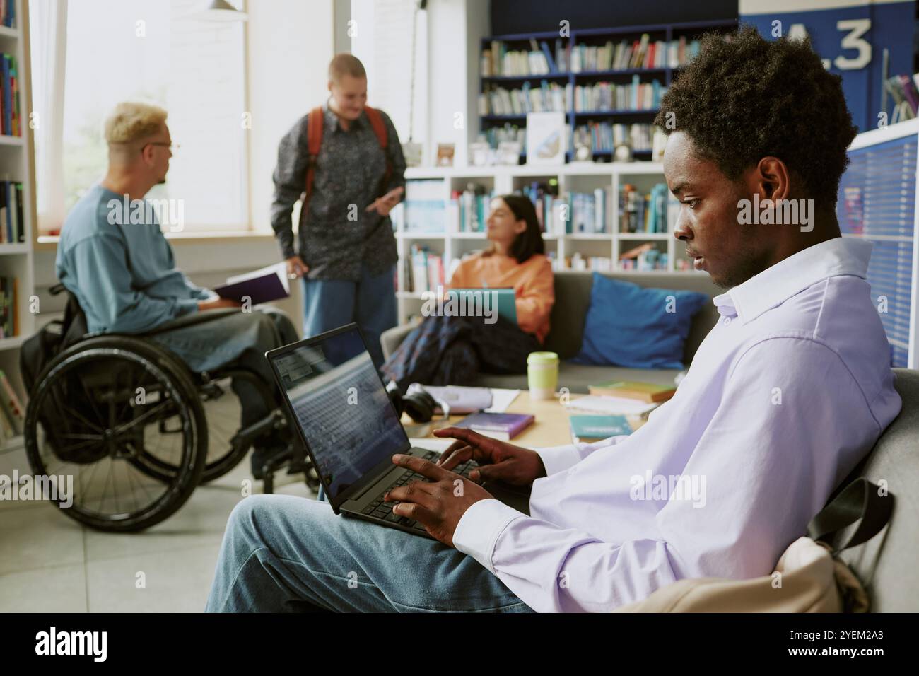 Membri di team di varie origini in un ambiente d'ufficio vivace e moderno, che collaborano a progetti. Scaffali, computer portatili e posti a sedere casual creano un ambiente coinvolgente per la discussione Foto Stock