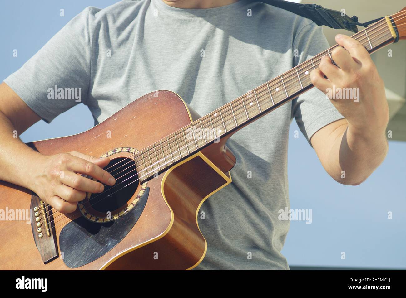 Un uomo suona accordi con una chitarra acustica senza scegliere. Un musicista durante una performance: Un primo piano di una chitarra e mani maschili che suonano le sue corde. Foto Stock