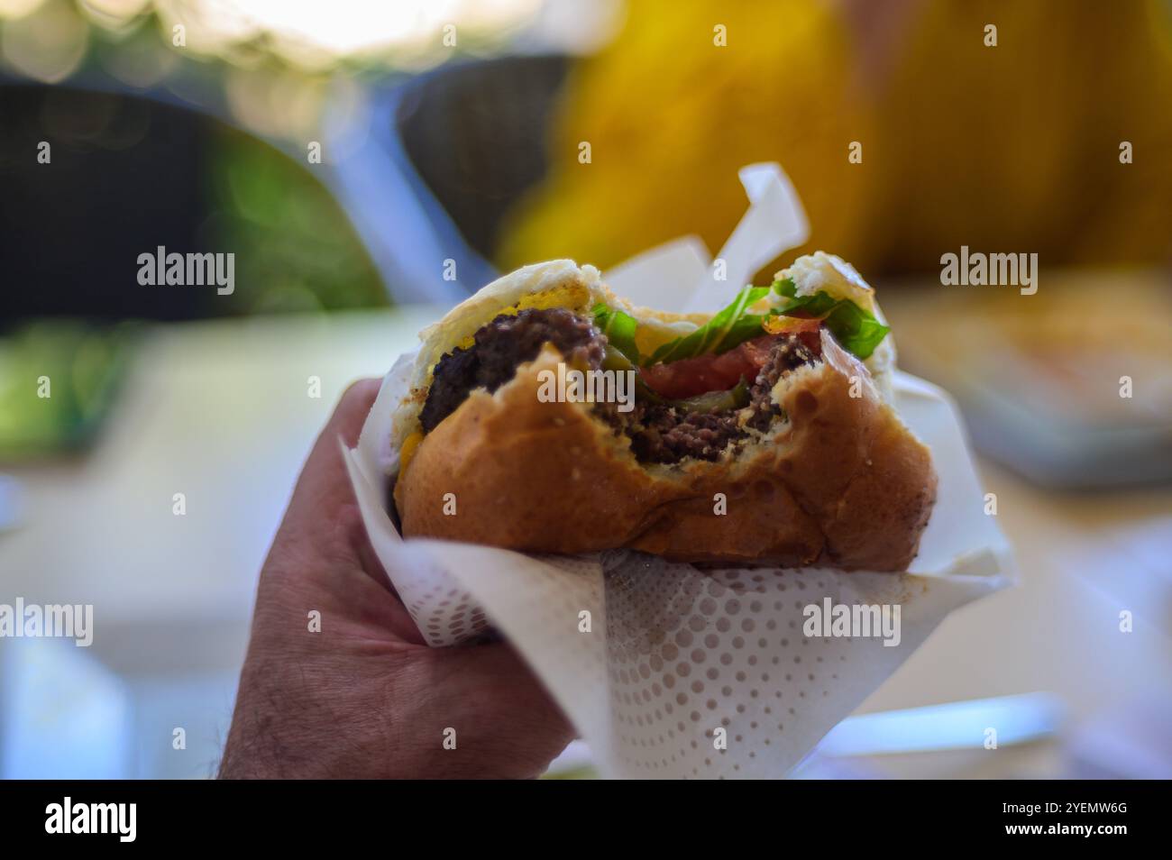 Una mano regge un succulento hamburger, ricco di ingredienti freschi, perfetto per un'esperienza culinaria informale. Foto Stock