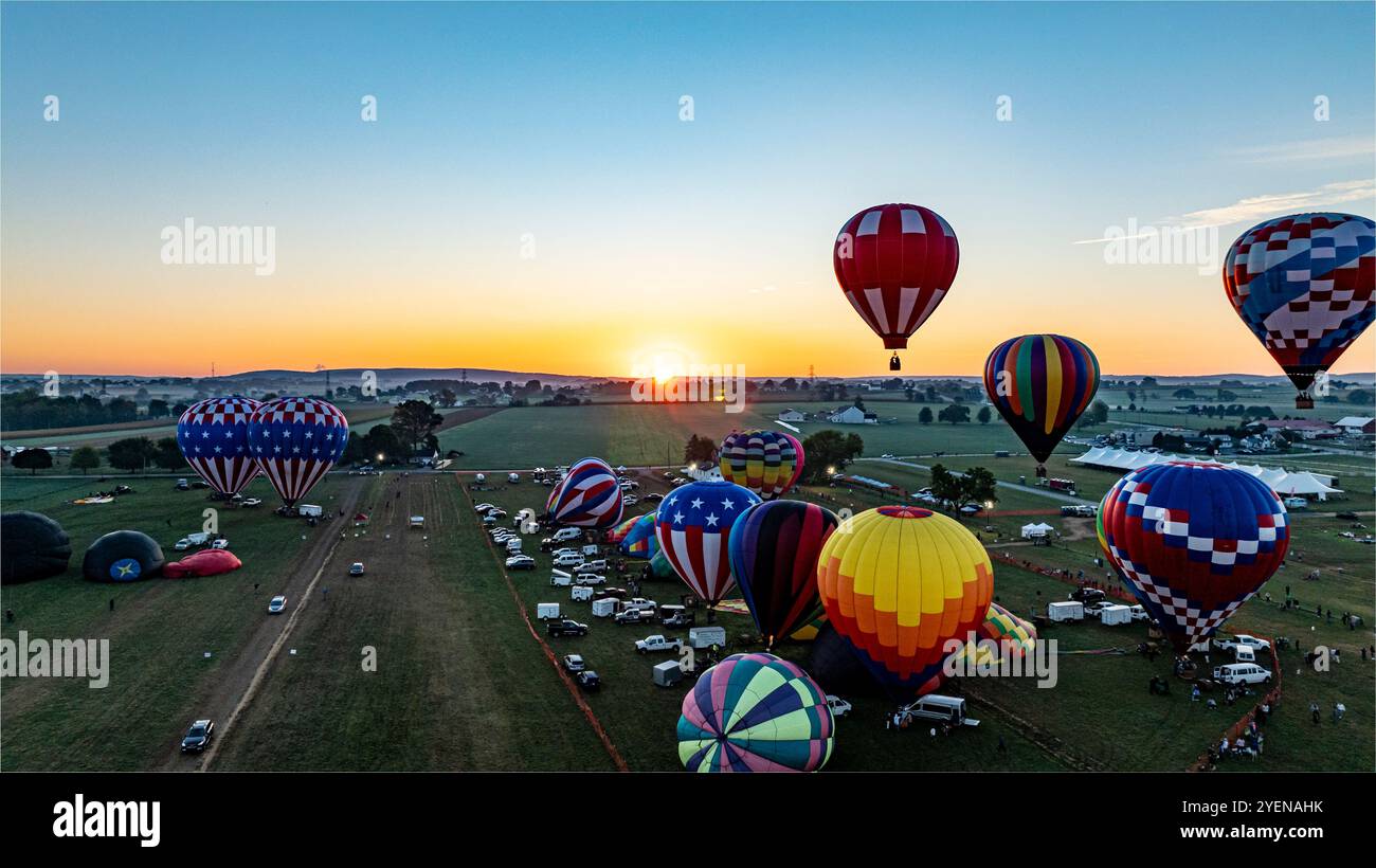 Una dozzina di colorate mongolfiere si stanno preparando per il lancio in un campo di festival durante il tramonto. Gli spettatori si riuniscono per assistere allo spettacolo come la sera Foto Stock