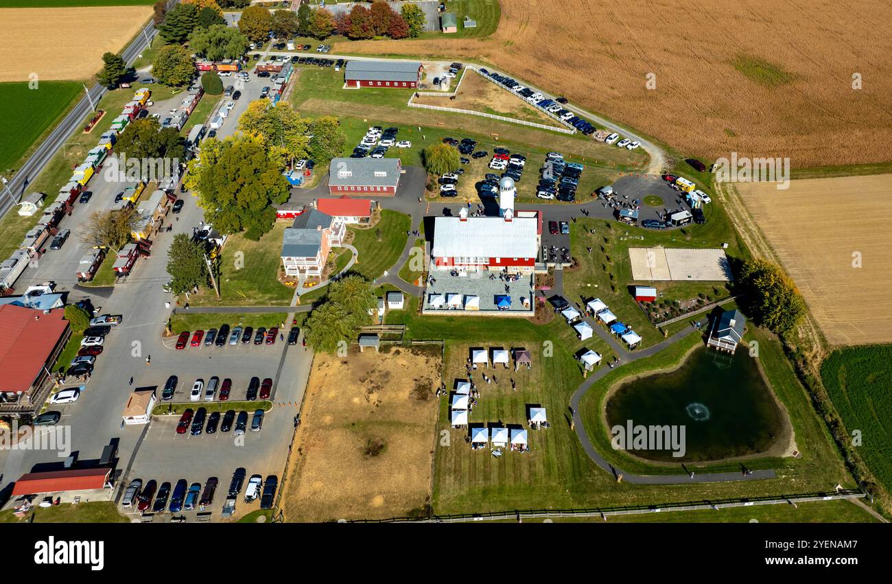 Una prospettiva aerea mostra una vivace area per eventi della comunità con tende e veicoli diversi parcheggiati nelle vicinanze, circondati da lussureggianti terreni agricoli, Highlighti Foto Stock