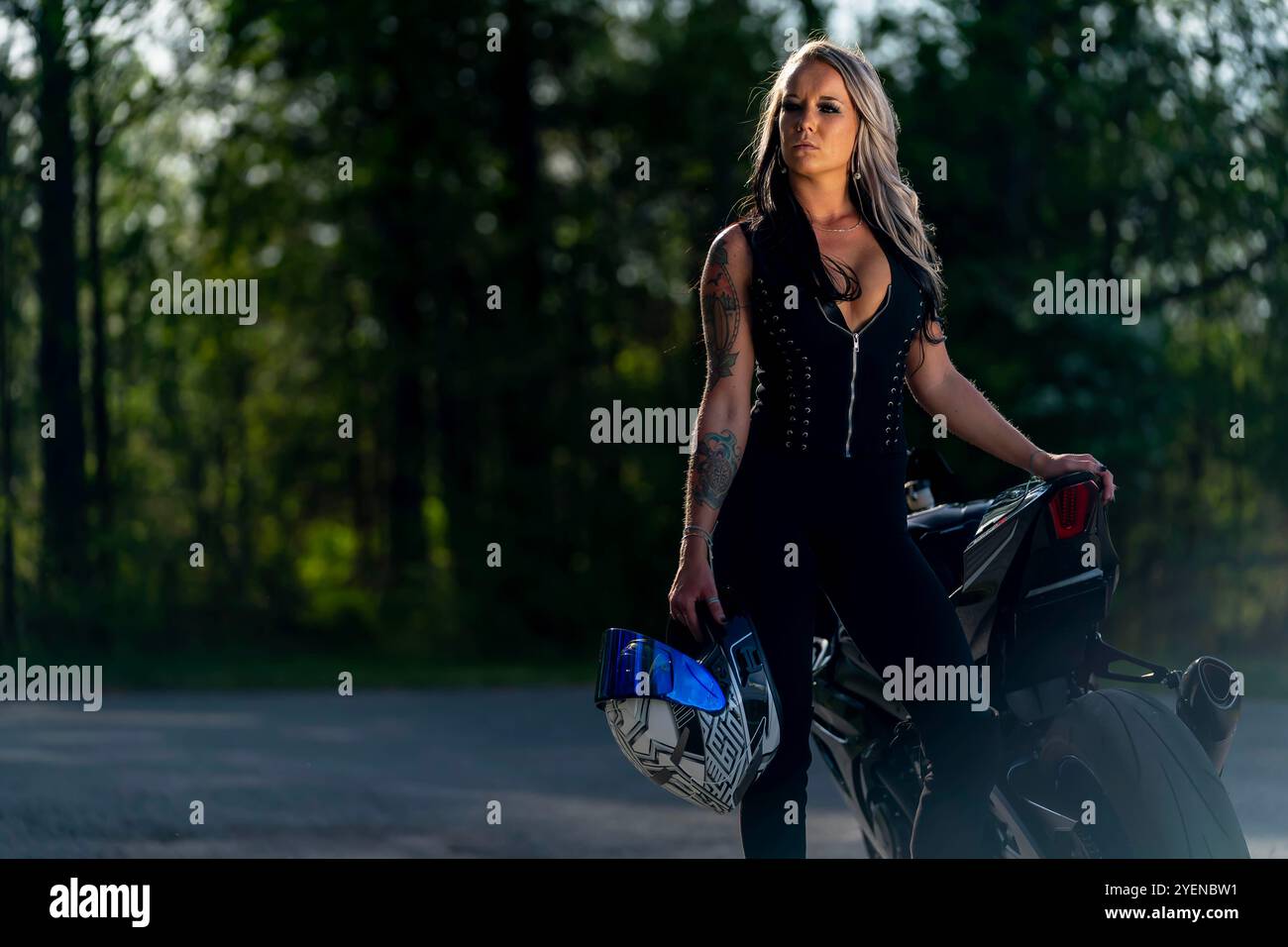 Una donna stupenda si mette in posa con sicurezza accanto alla sua moto ad alte prestazioni. Con uno sguardo feroce e una posizione avvolta, irradia potenza e passione Foto Stock