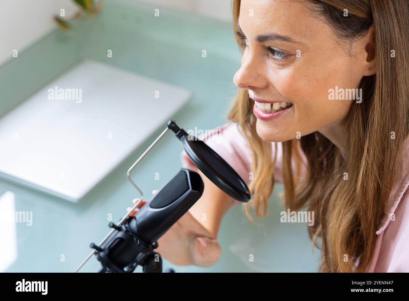 Donna sorridente che registra podcast a casa con configurazione professionale del microfono. Podcasting, trasmissione, audio, apparecchiature, storytelling, creazione di contenuti Foto Stock