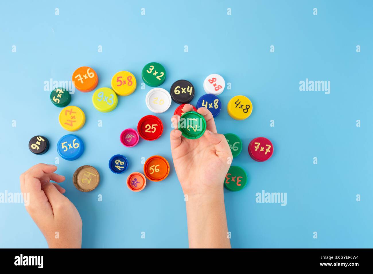 attività di matematica per bambini, gioco per bambini, allenamento matematico, apprendimento della tabella di moltiplicazione riutilizzando tappi di plastica, vista dall'alto sfondo blu Foto Stock