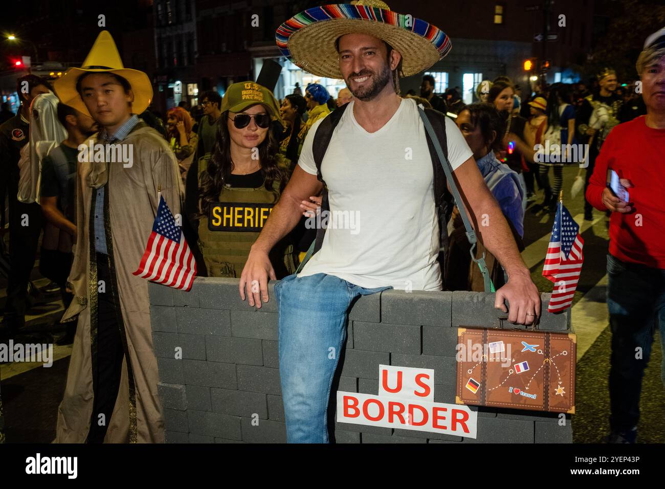 New York, New York, Stati Uniti. 31 ottobre 2025. La parata annuale di Halloween del Greenwich Village ha attirato folle di partecipanti in costume insieme a band, compagnie di danza, camminatori palafitte, carri commerciali e marionette giganti all'evento a tema "Meow!!!" in una mite serata autunnale. Un uomo indossa un sombrero di paglia e cerca di oltrepassare un muro al confine tra Stati Uniti e Messico mentre un agente dell'immigrazione lo tiene in braccio. Crediti: Ed Lefkowicz/Alamy Live News Foto Stock