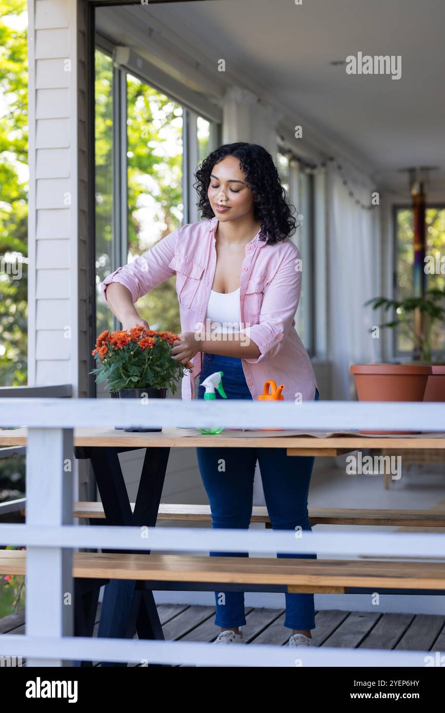 Donna che cura le piante sul portico, si gode il giardinaggio in uno spazio all'aperto soleggiato. orticoltura, luce del sole, fine settimana, relax Foto Stock