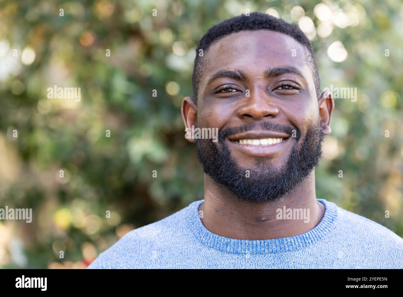 Uomo afro-americano sorridente che si gode una giornata autunnale all'aperto, indossa un comodo maglione blu, copia spazio. natura, stagione, clima, fogliame, moda Foto Stock
