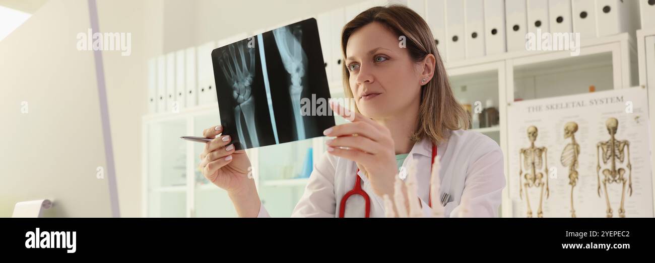 Il medico studia l'immagine radiografica del braccio del paziente seduto alla scrivania Foto Stock