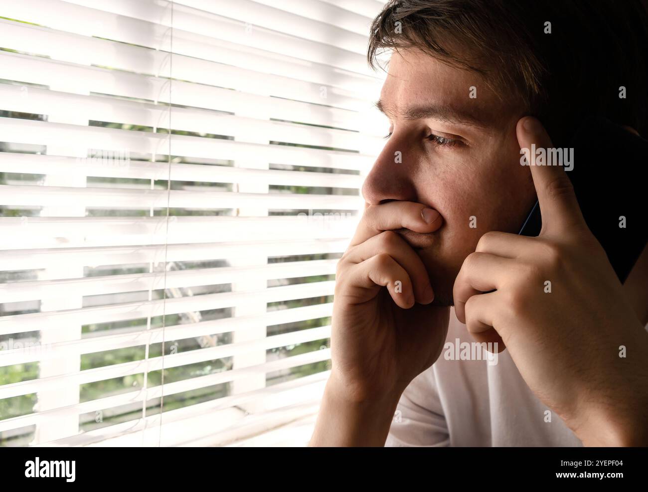 Uomo giovane triste vicino alla finestra nella stanza Foto Stock