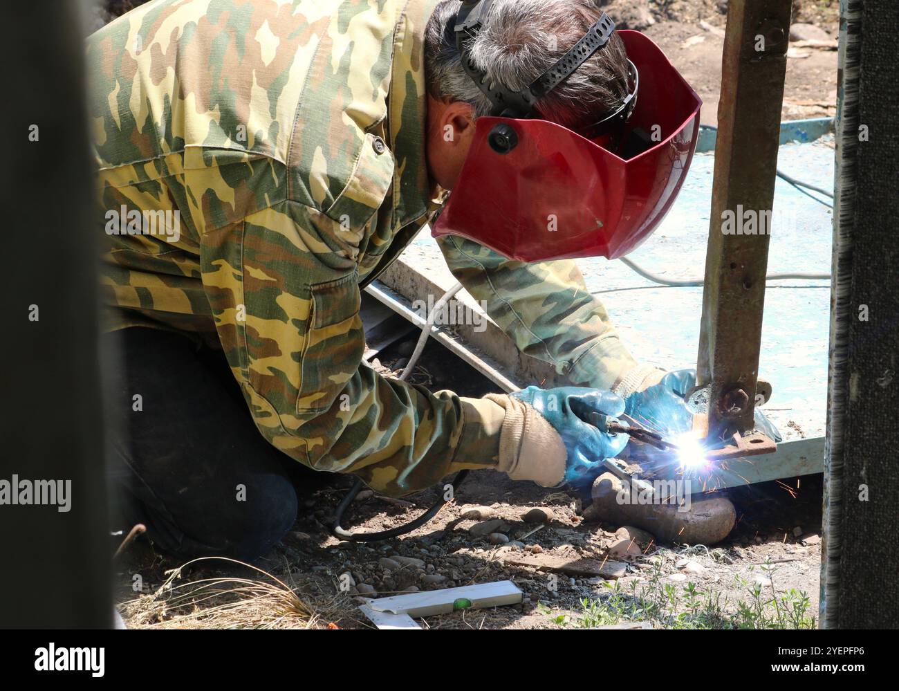 saldatrice che unisce le parti di un tavolo di metallo mediante saldatura, saldatura di una gamba di ferro su una superficie utilizzando una saldatrice, lavoro di uno specialista di saldatura Foto Stock